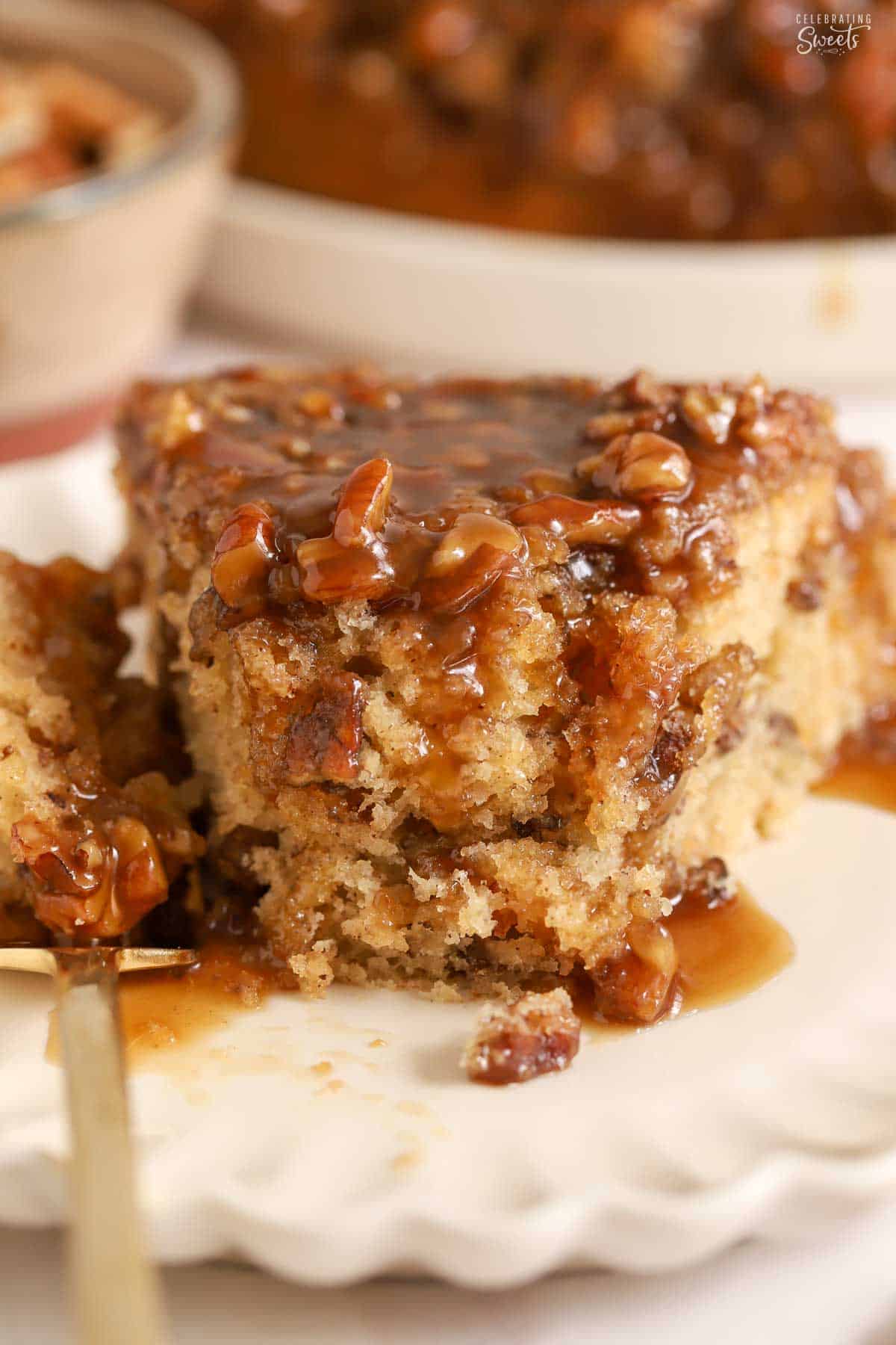 Slice of pecan pie cake with caramel sauce on a white scalloped plate.