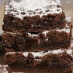 Stacked of three chocolate cookie bars topped with powdered sugar.