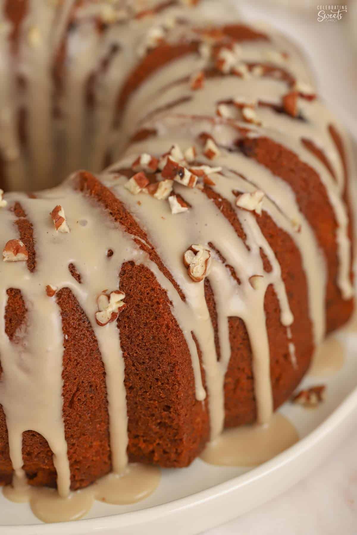 Closeup of a bundt cake topped with brown icing and pecans on a white plate.