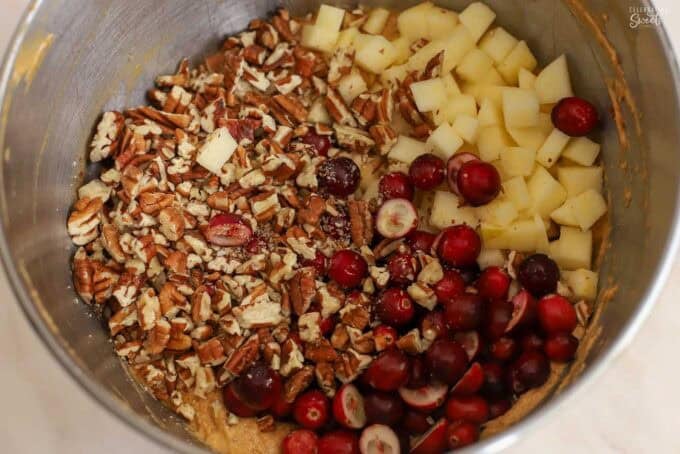 Pecans, cranberries, and apples on top of cake batter in a metal bowl.