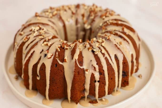 A bundt cake topped with light brown icing and pecans on a white plate.