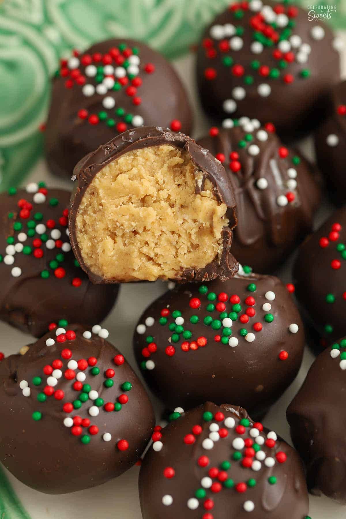 Chocolate covered peanut butter balls topped with red, white, and green sprinkles on a green plate.