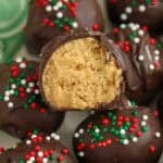 Chocolate covered peanut butter balls topped with red, white, and green sprinkles on a green plate.