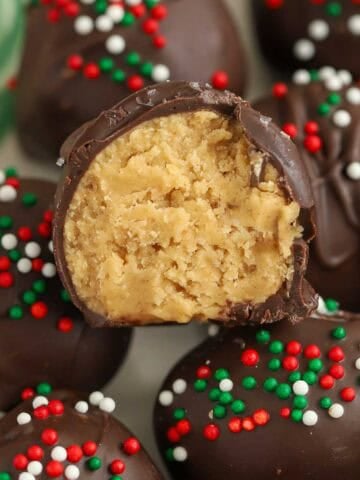 Chocolate covered peanut butter balls topped with red, white, and green sprinkles on a green plate.
