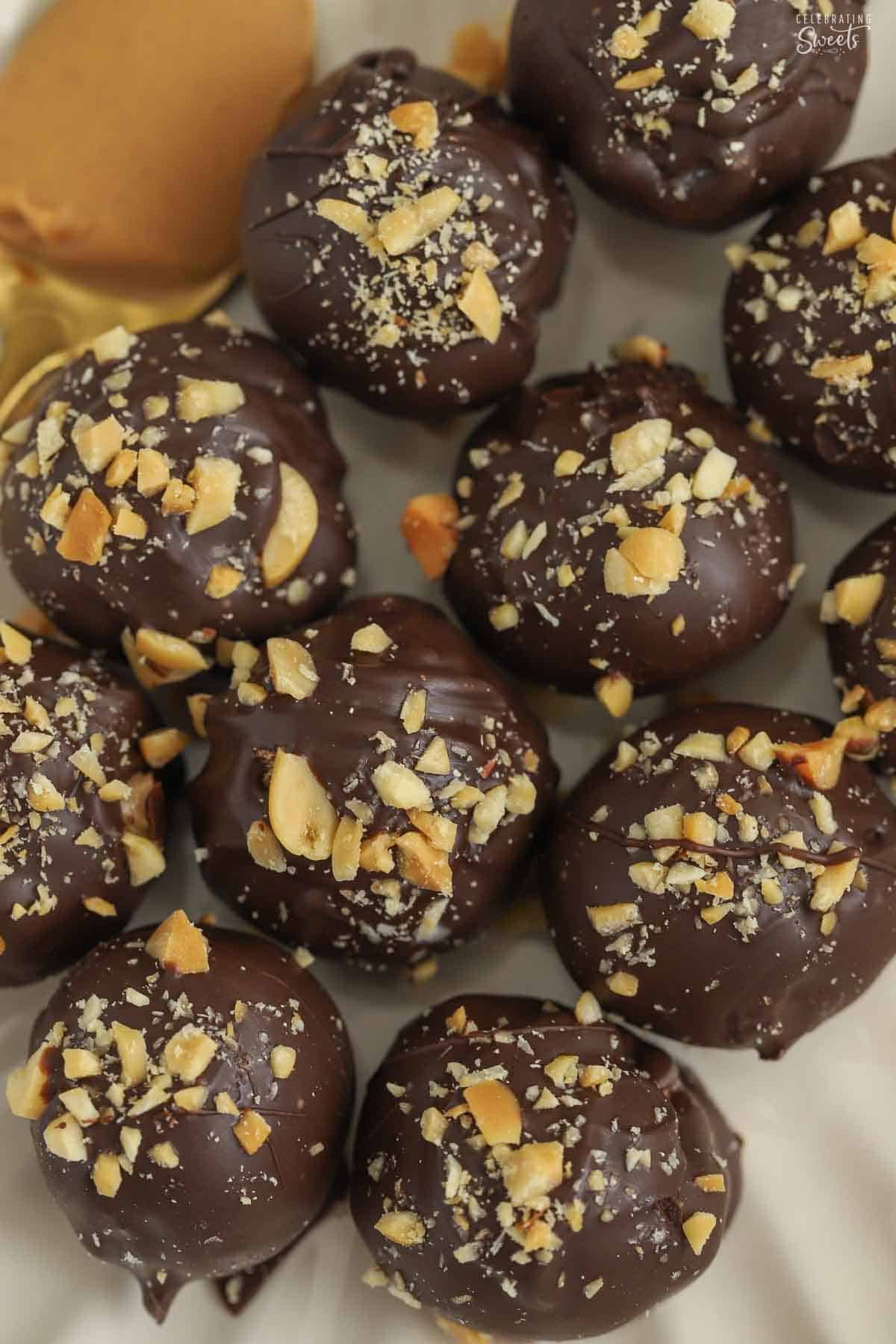 A white plate of chocolate covered peanut butter balls topped with chopped peanuts.