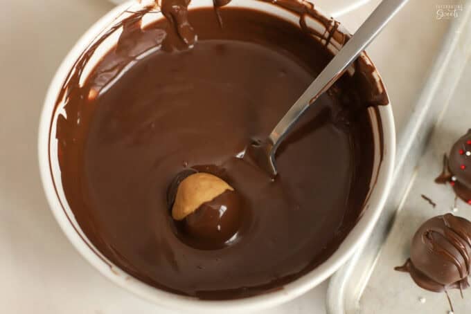 A peanut butter ball on a fork being dipped into a bowl of melted chocolate.