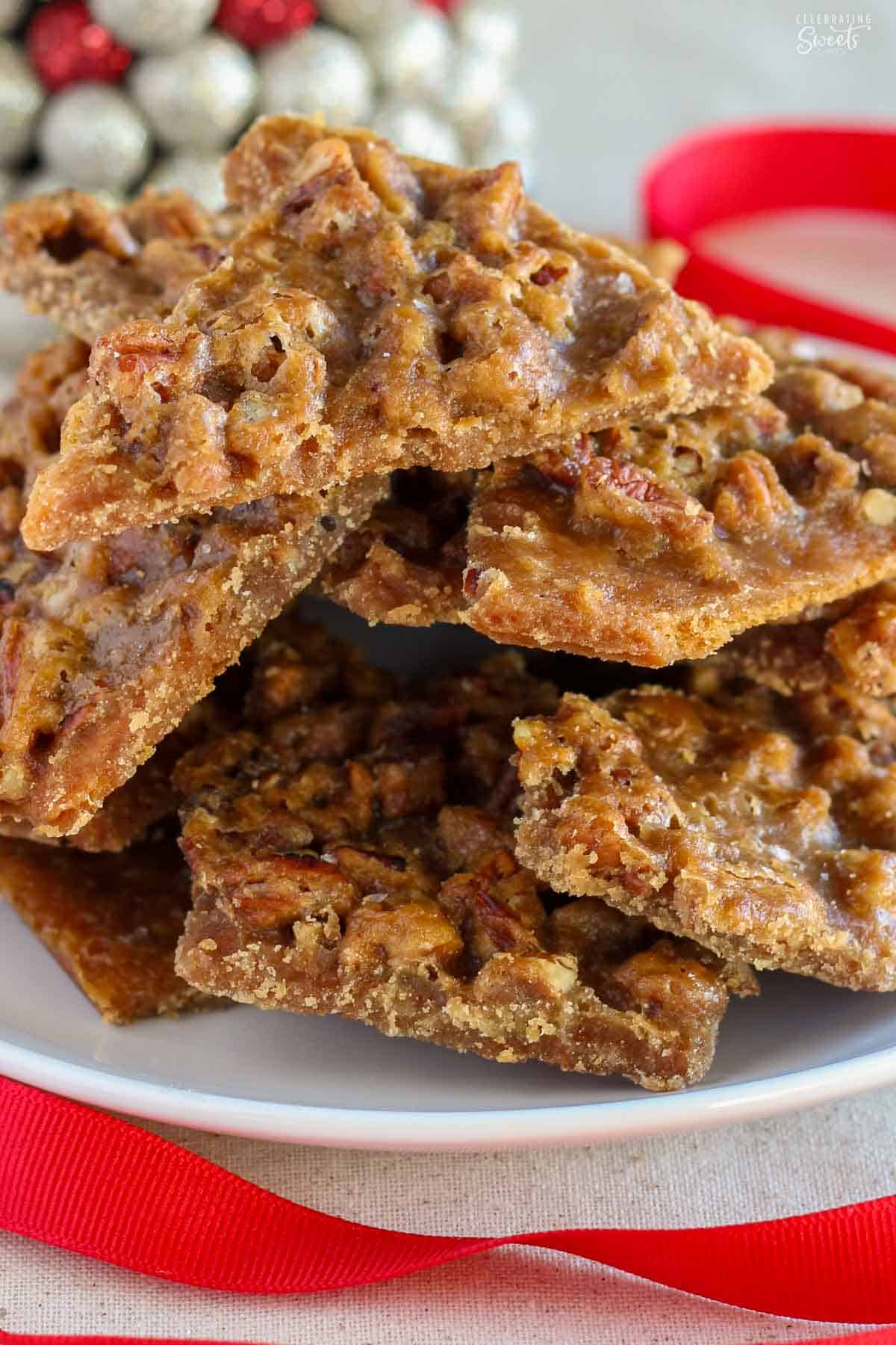 Pecan praline toffee piled on a white plate next to a red ribbon.
