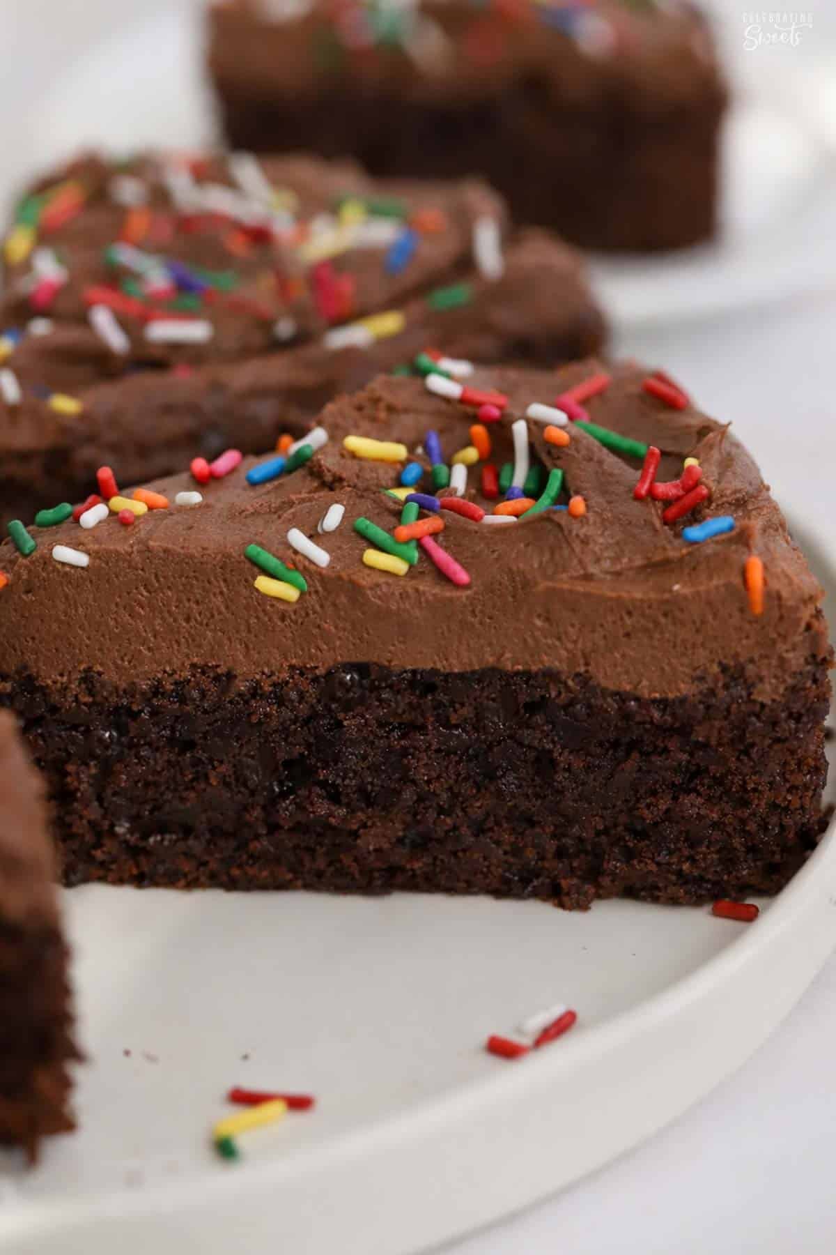 A slice of brownie cake topped with chocolate frosting and rainbow sprinkles.