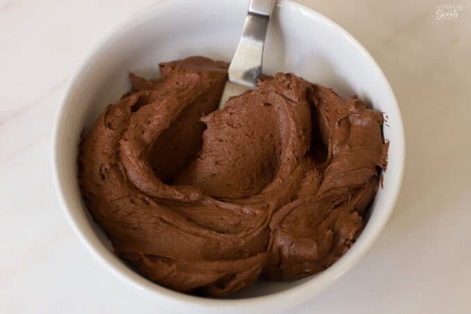 Chocolate frosting in a white bowl with a small offset spatula.