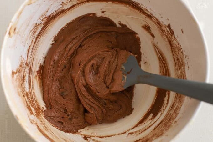 Brownie batter in a white bowl with a grey spatula.