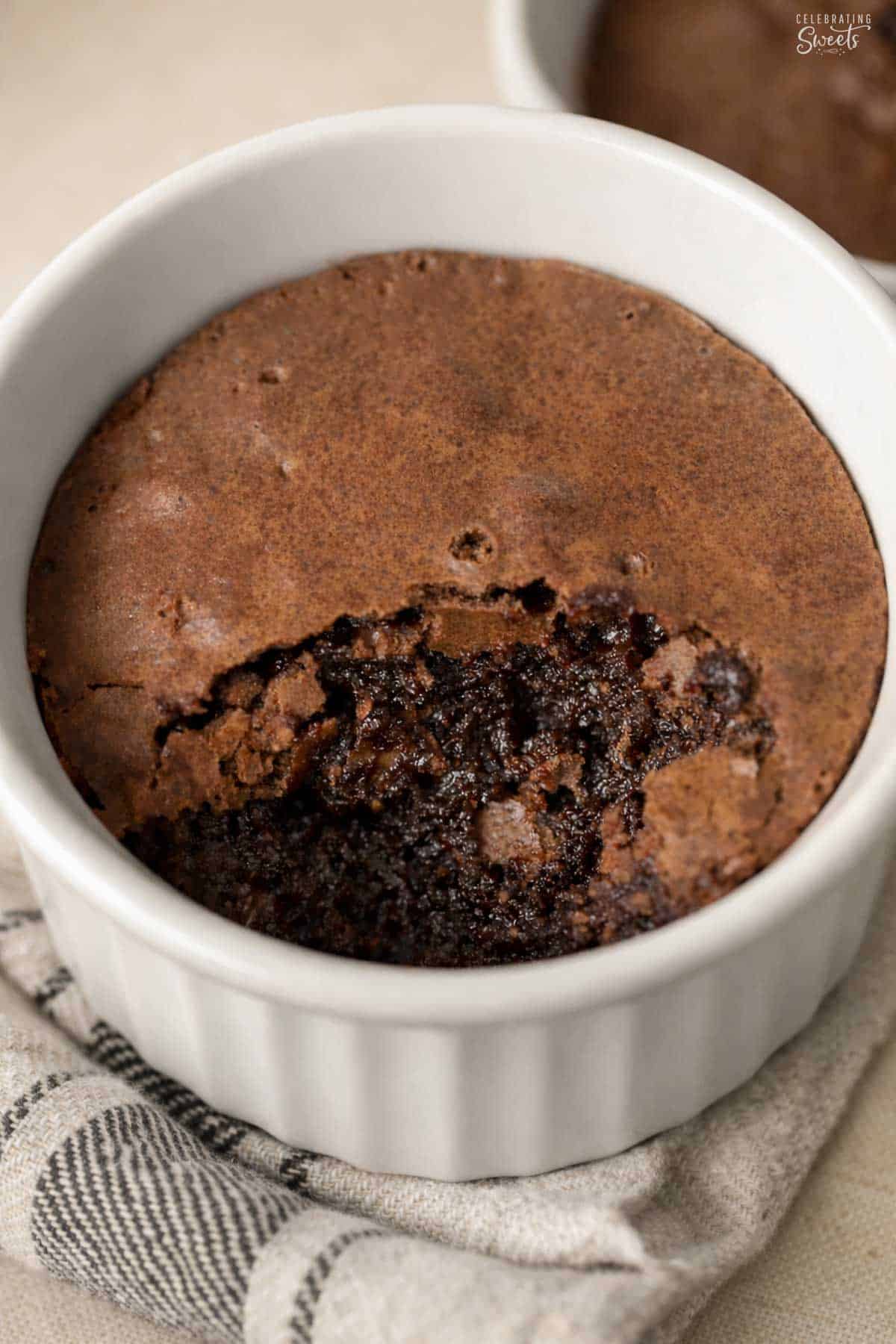 Brownie pudding in a white ramekin sitting on a grey towel.
