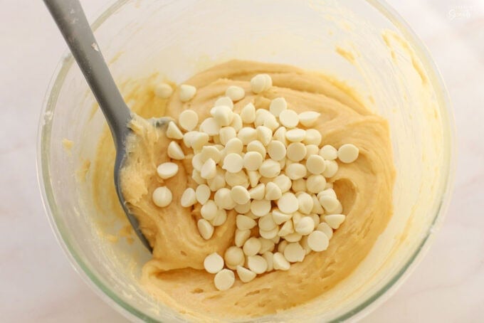 Lemon brownie batter in a glass bowl with white chocolate chips.