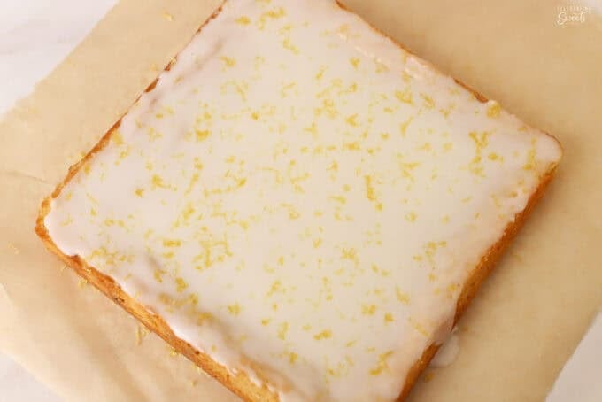 Uncut lemon brownie topped with white icing and lemon zest on a piece of parchment paper.