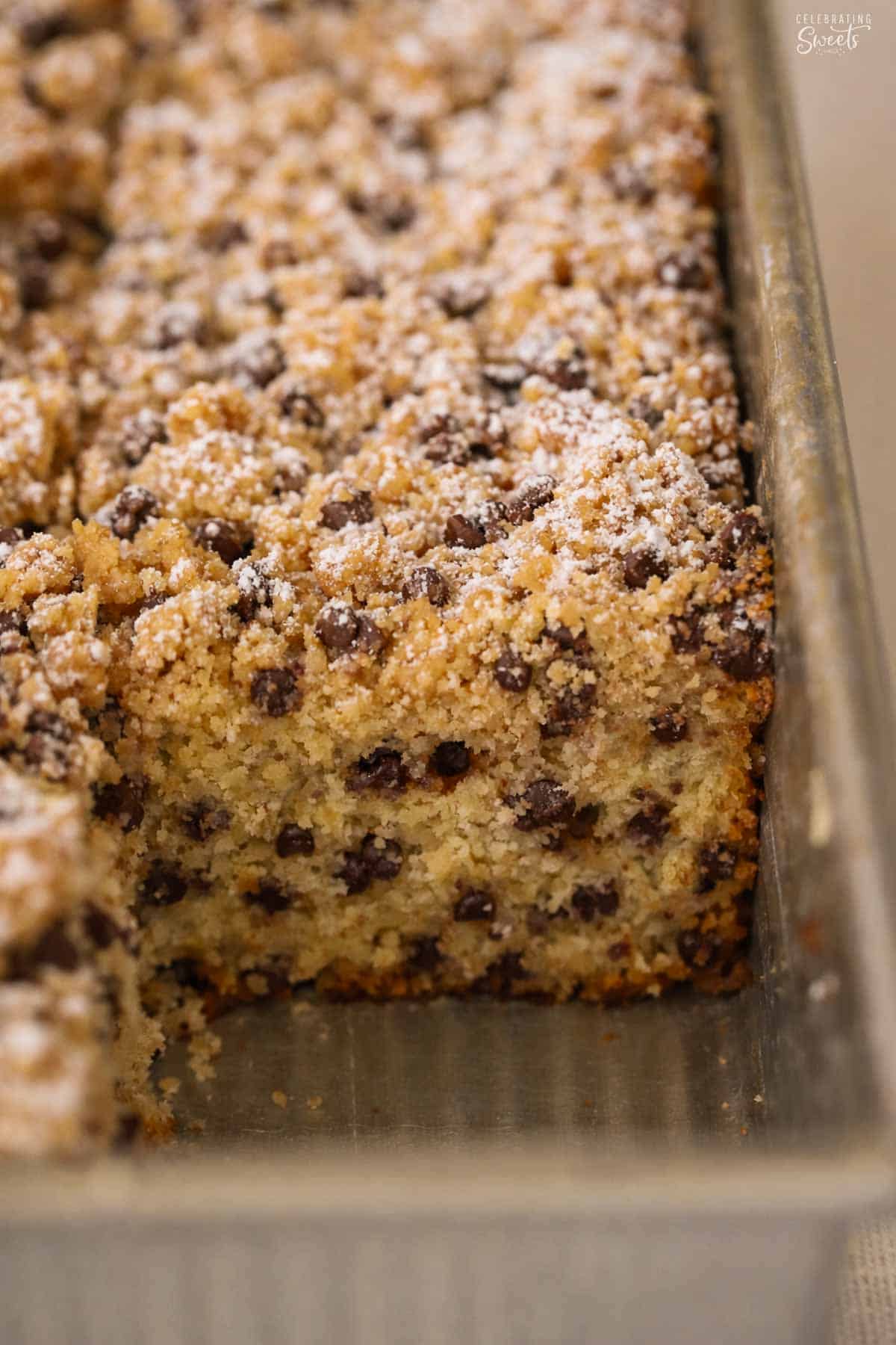 Chocolate chip crumb cake in a metal pan dusted with powdered sugar.