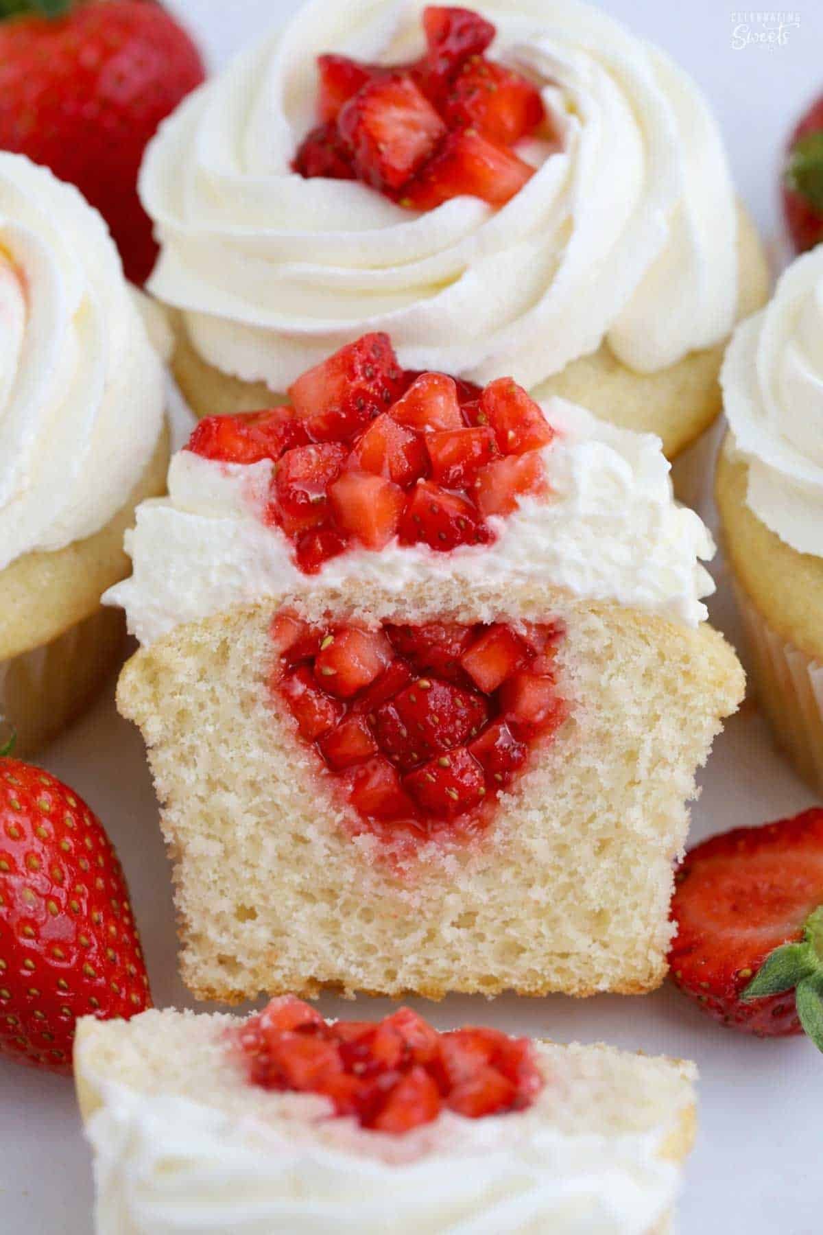 Strawberry shortcake cupcake cut in half, filled with diced strawberries, and topped with white frosting and strawberries.