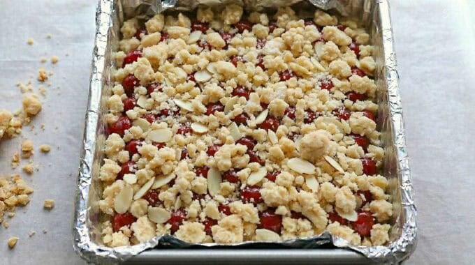 Unbaked cherry crumb bars in a foil-lined baking pan.