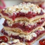 Stack of three cherry crumble bars on a piece of parchment.