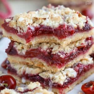 Stack of three cherry crumble bars on a piece of parchment.