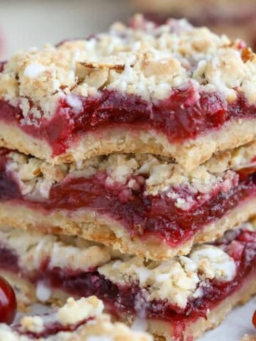 Stack of three cherry crumble bars on a piece of parchment.