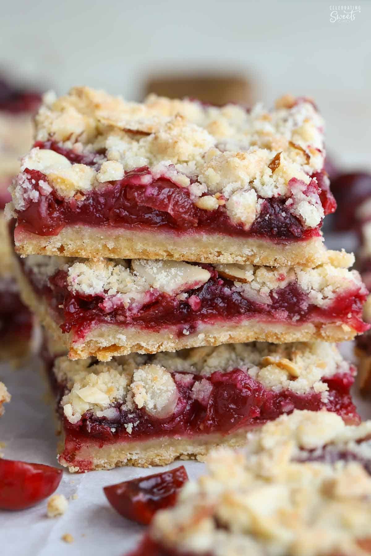 Stack of three cherry crumble bars next to two fresh cherries.