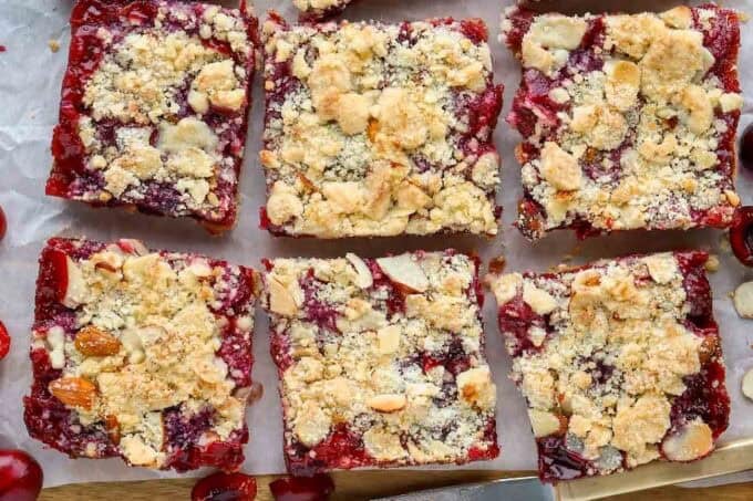 Six cherry crumb bars on parchment paper.