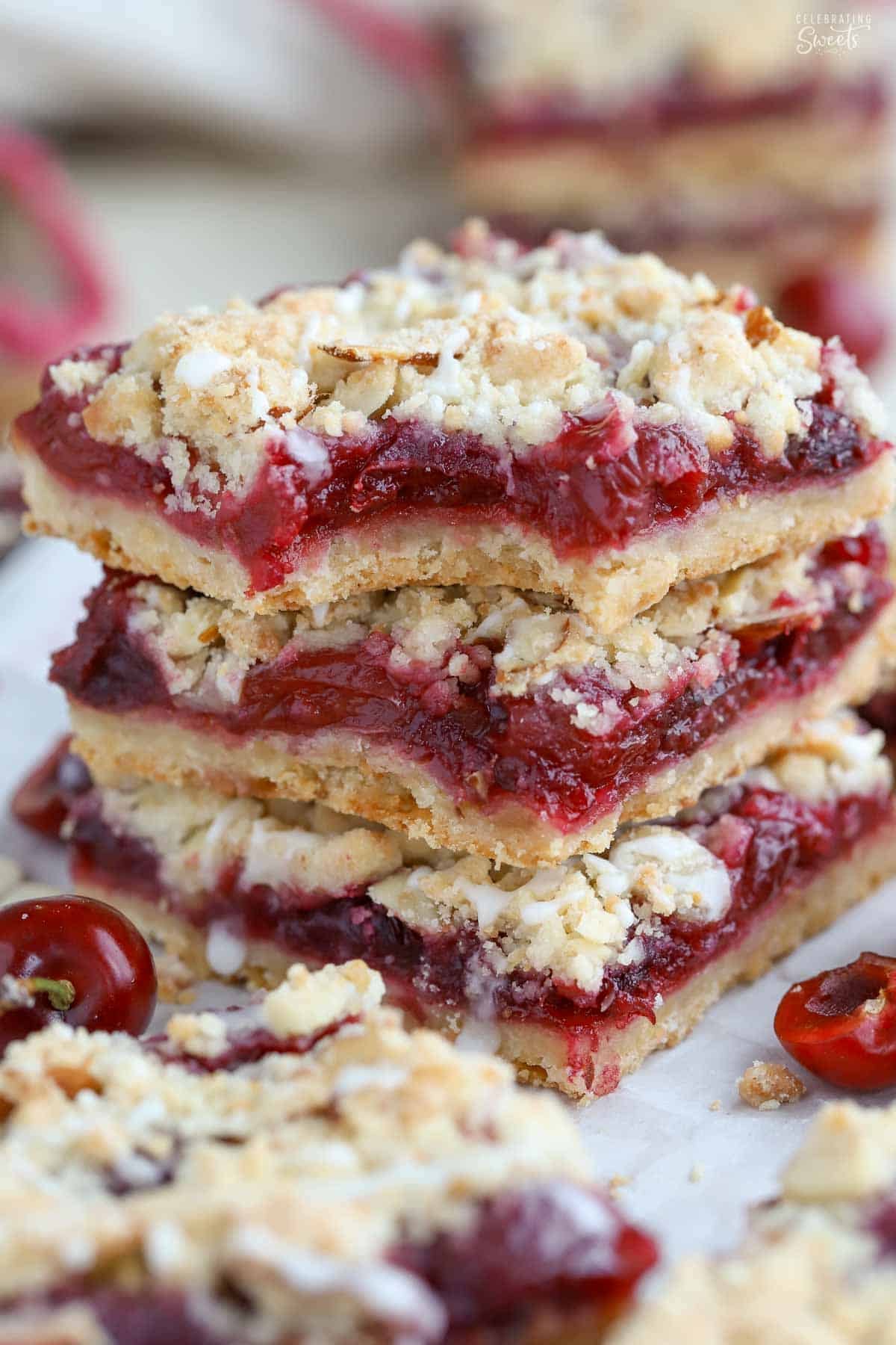 Stack of three cherry crumble bars on a piece of parchment.