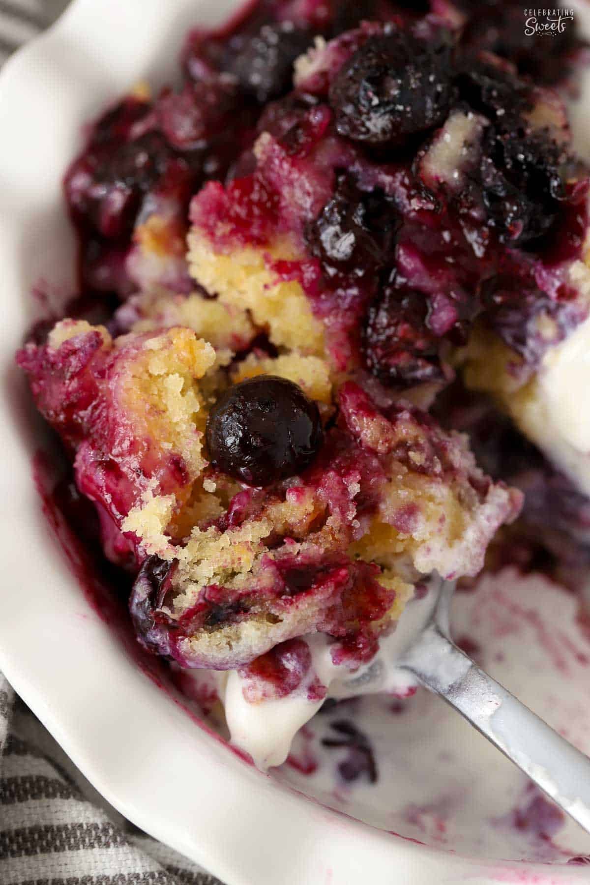 A scoop of lemon cake and blueberries on a spoon in a white bowl.