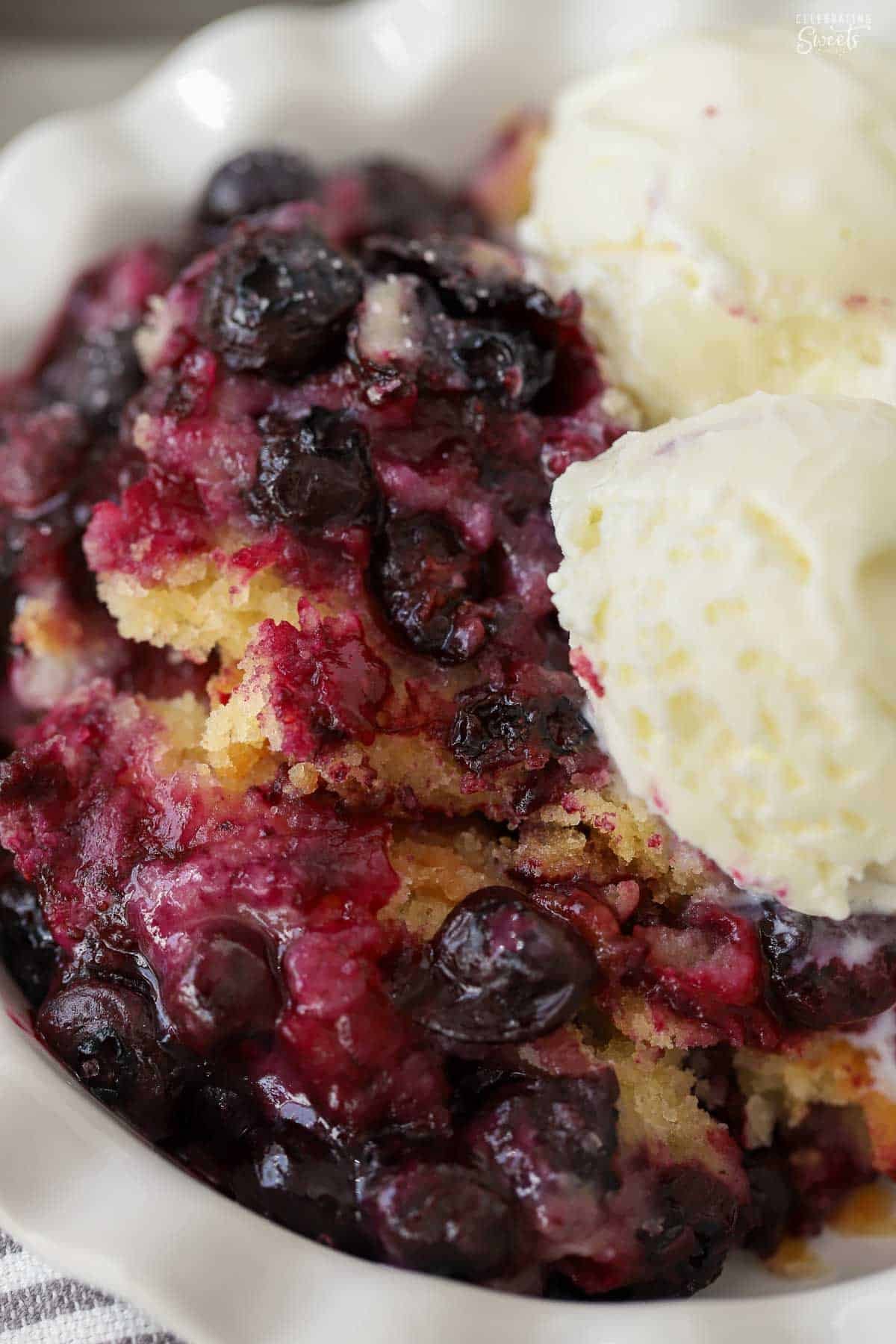 Lemon blueberry spoon cake in a white bowl topped with ice cream.