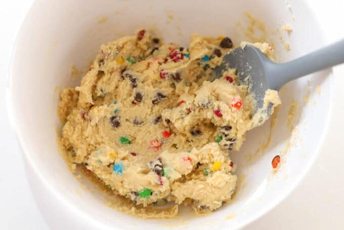 M&M cookie dough in a white bowl with a grey spatula.