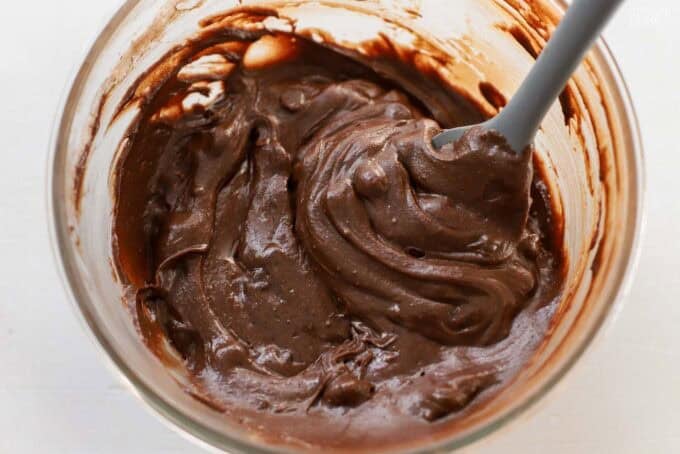 Brownie batter in a glass bowl with a grey rubber spatula.
