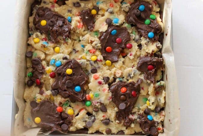 Unbaked M&M brookies in a parchment-lined square baking pan,