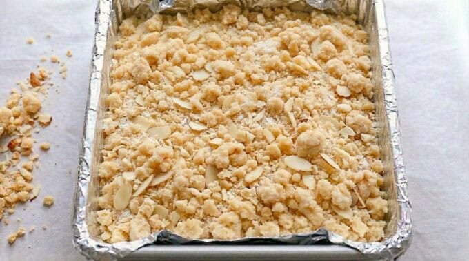 Almond cheesecake bars in a foil-lined square pan.