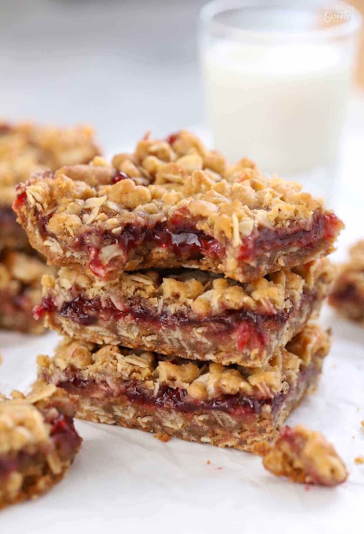 Stack of three oatmeal jam bars on a piece of parchment paper.