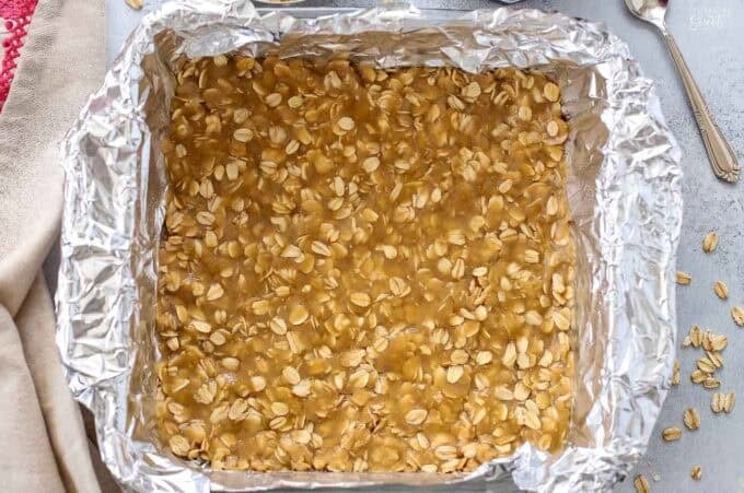 Oatmeal cookie dough pressed into the bottom of a foil-lined baking dish.
