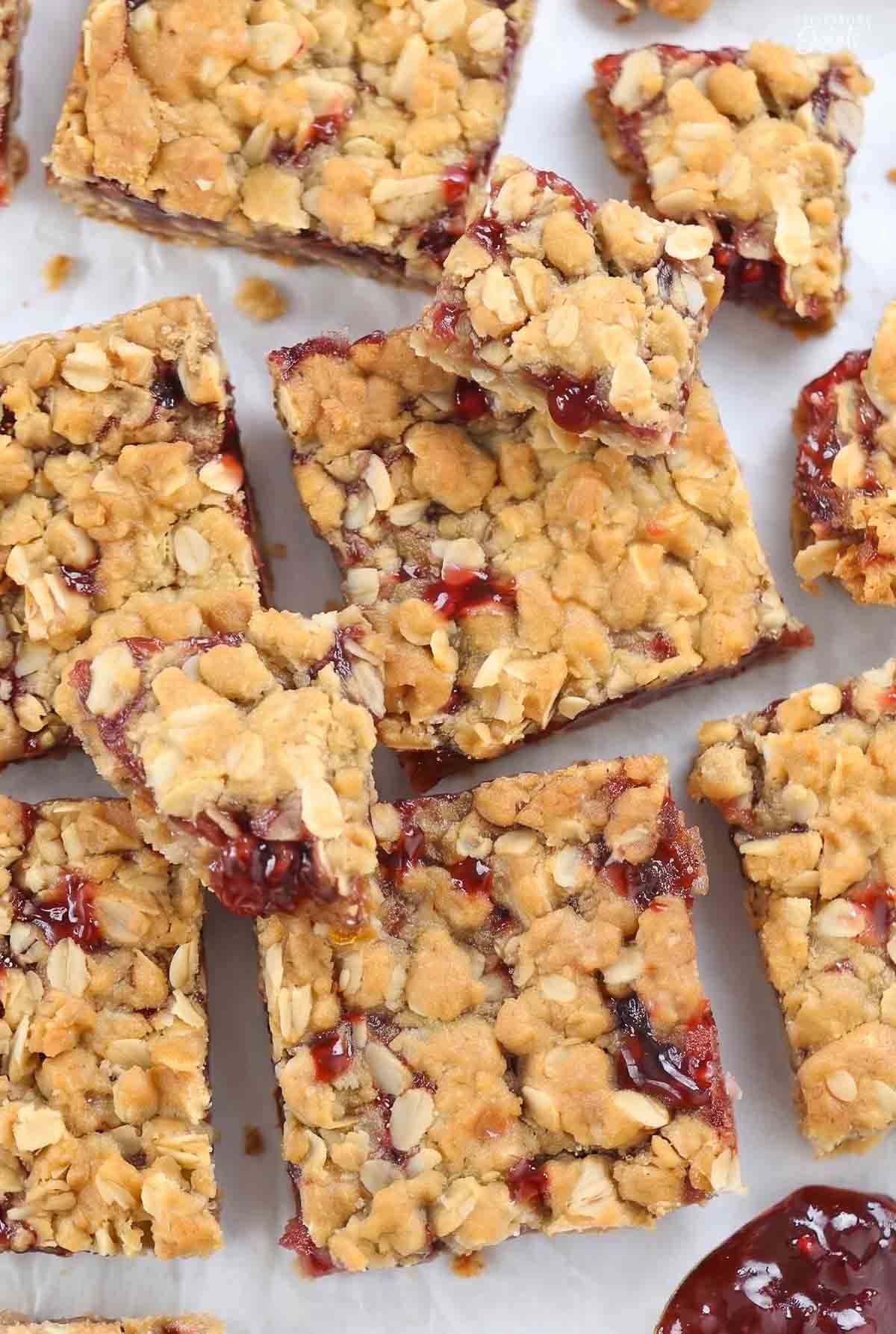 Oatmeal jam bars on parchment paper next to a spoon with jam on it.