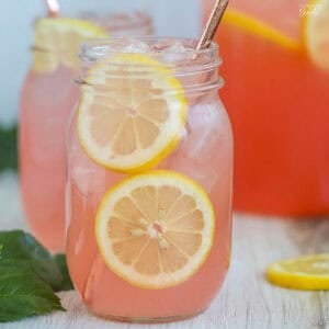 Two glass mason jars of pink lemonade with sliced lemonade garnishes.