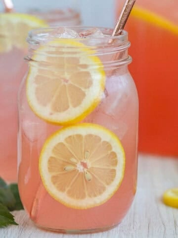 Two glass mason jars of pink lemonade with sliced lemonade garnishes.