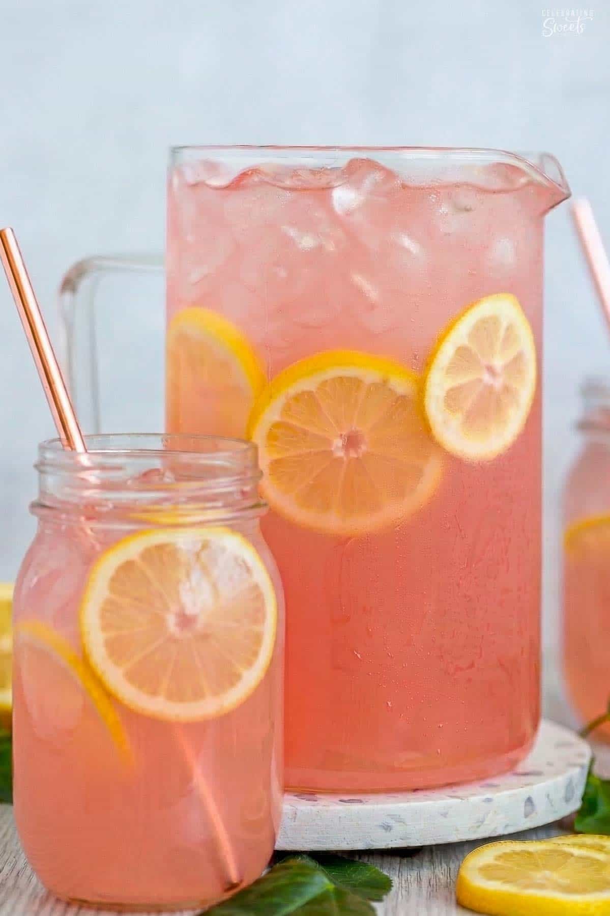 A pitcher of pink lemonade with a glass jar of lemonade sitting in front of it.