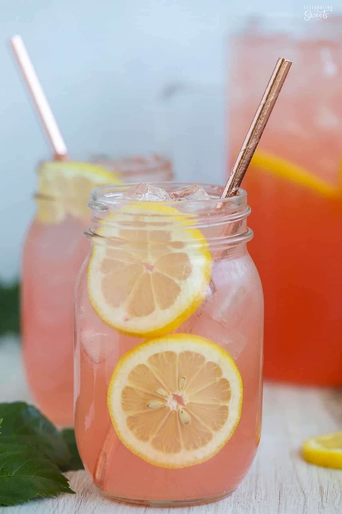Two glass mason jars of pink lemonade with sliced lemonade garnishes.