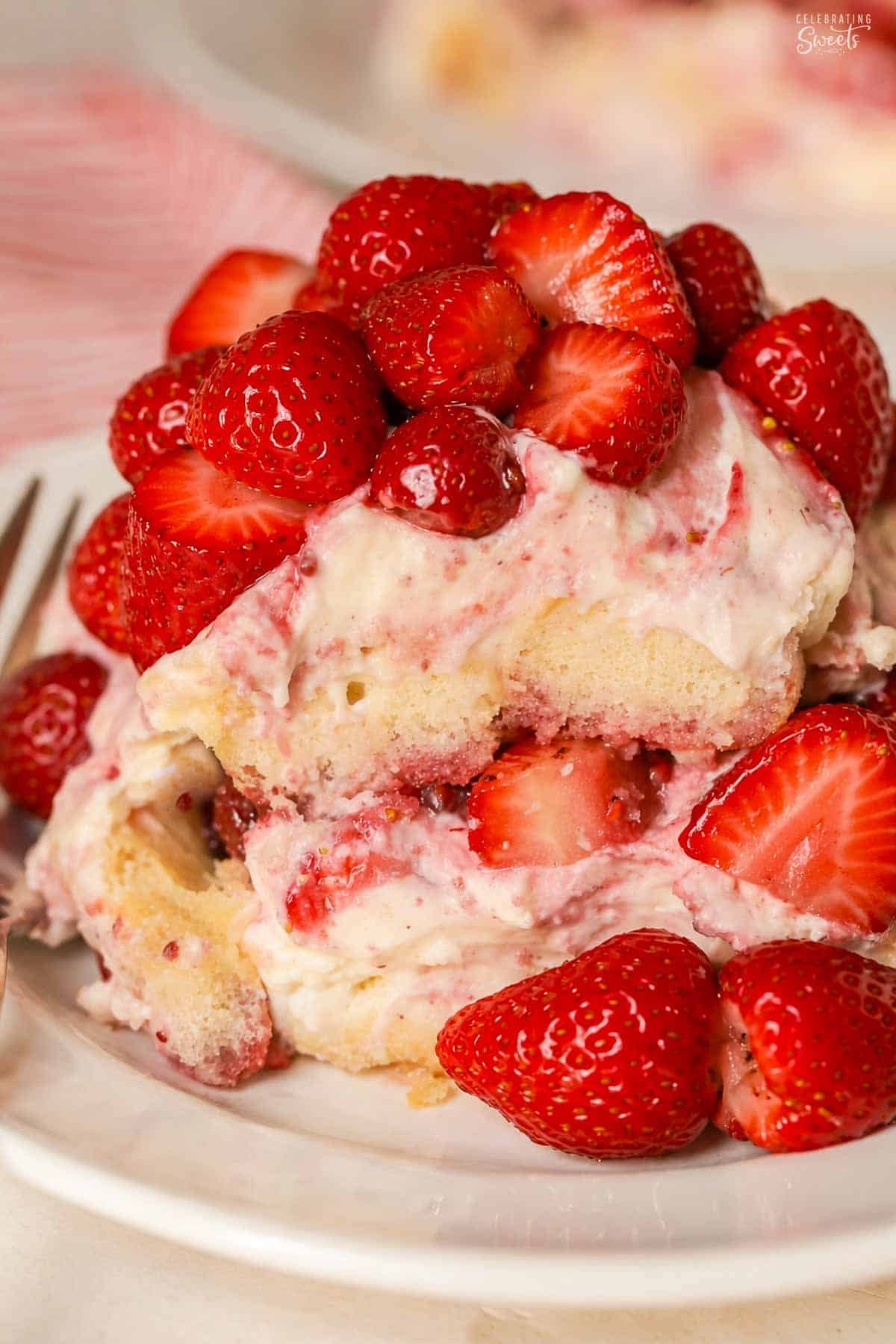 A serving of strawberry tiramisu on a round white plate with a gold fork on it.