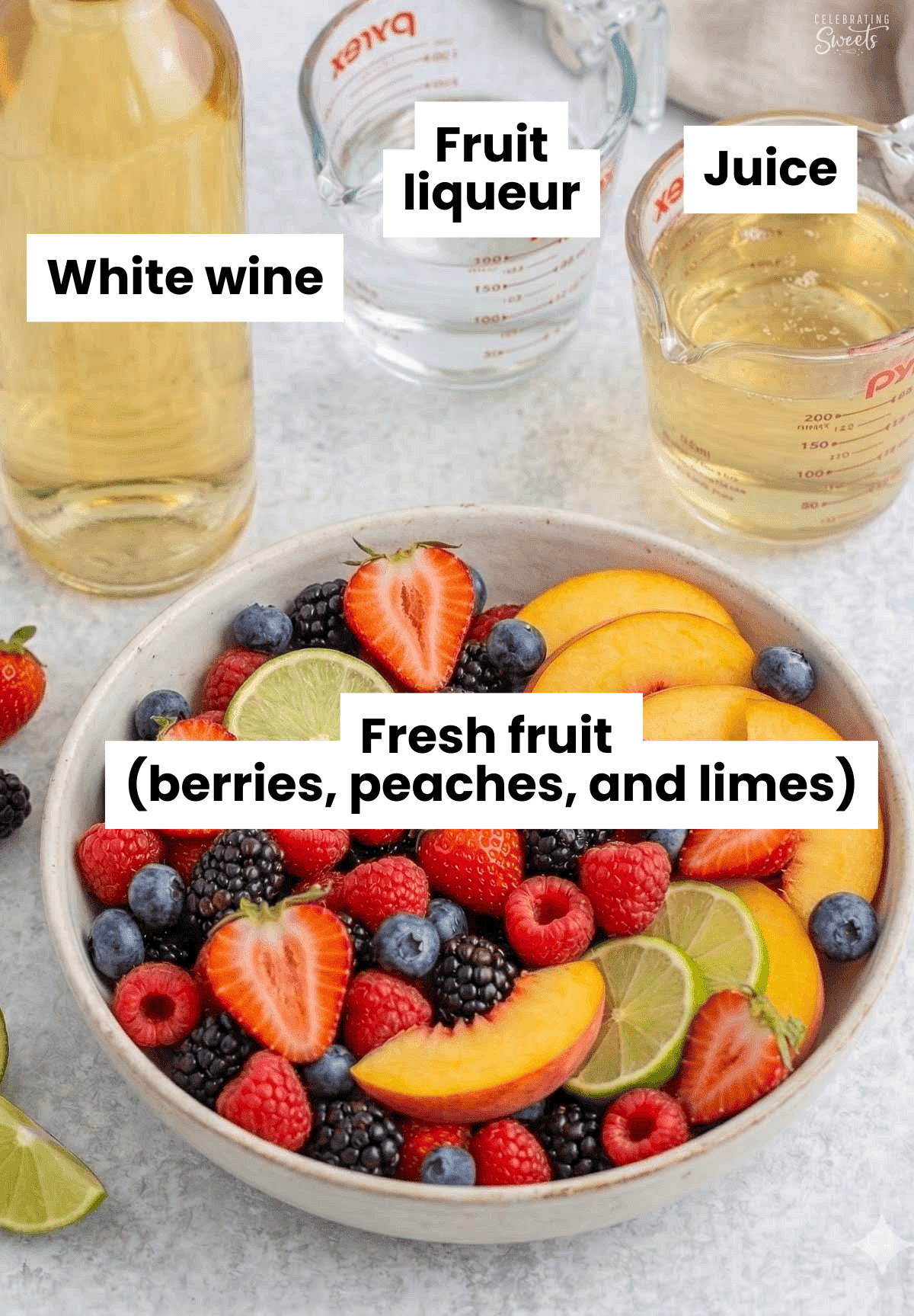 Ingredients for white sangria (bowl of fresh fruit. bottle of white wine, glass measuring cups filled with juice and liqueur).