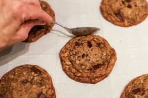 A spoon pressing into the outer edge of a cookie on a baking sheet.