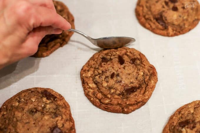 A spoon pressing into the outer edge of a cookie on a baking sheet.