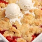 Strawberry cobbler in a white baking dish topped with two scoops of vanilla ice cream.