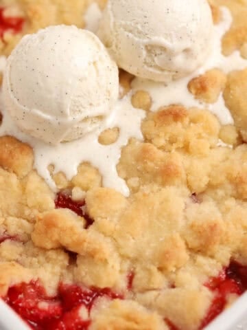 Strawberry cobbler in a white baking dish topped with two scoops of vanilla ice cream.