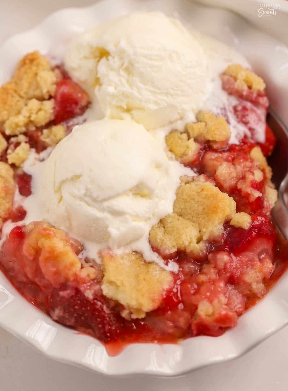 Strawberry cobbler in a white bowl topped with two scoops of vanilla ice cream.