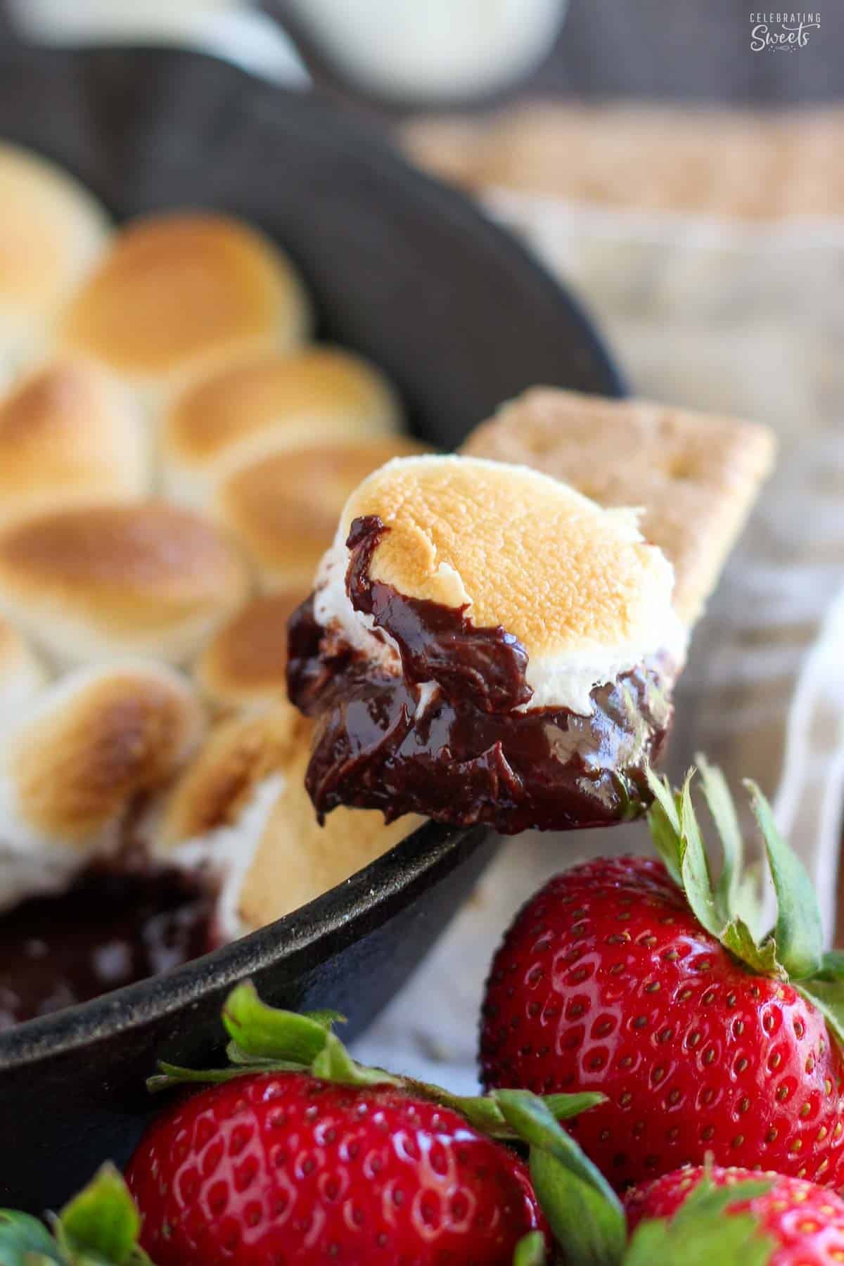 A graham cracker topped with s'mores dip sitting on the side of a cast iron skillet.