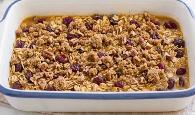 Pumpkin oatmeal in a blue and white baking dish topped with pecans and dried cranberries.