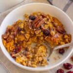 A white bowl filled with pumpkin oatmeal, pecans, and dried cranberries.