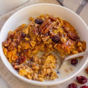 A white bowl filled with pumpkin oatmeal, pecans, and dried cranberries.